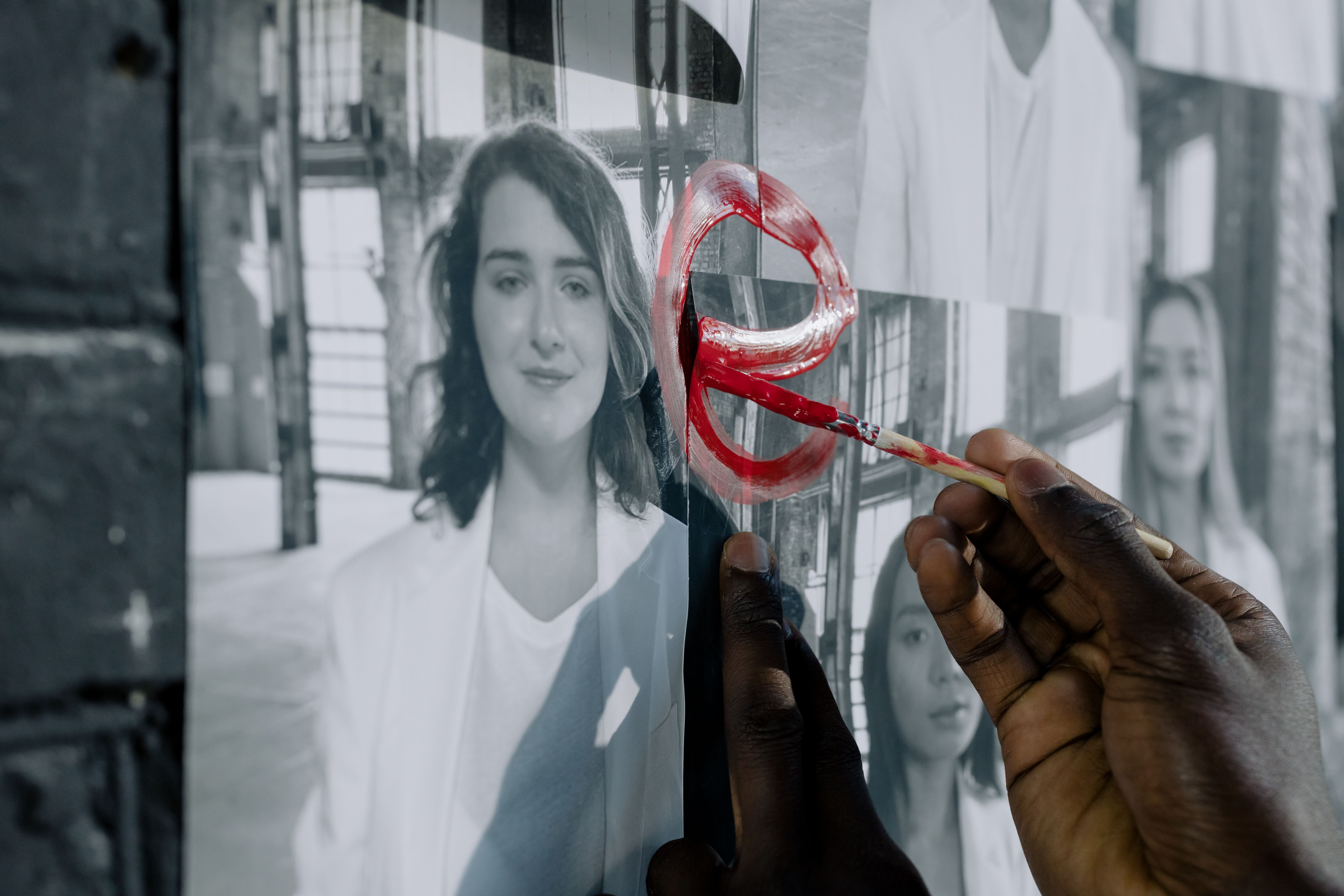 A hand painting red symbols on black and white photos, emphasizing artistic expression.