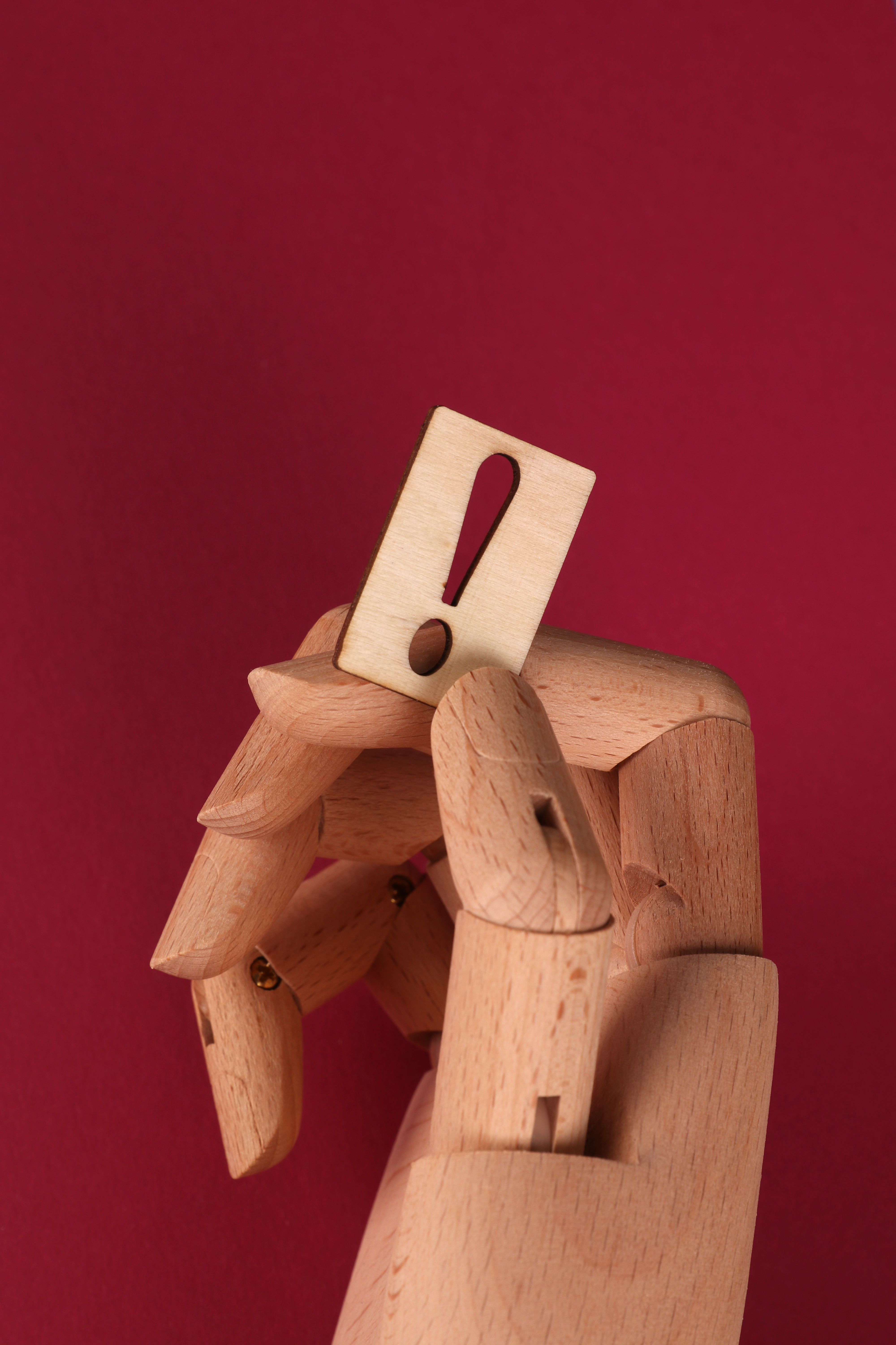 Conceptual image of a wooden hand holding an exclamation mark on a vibrant red background.