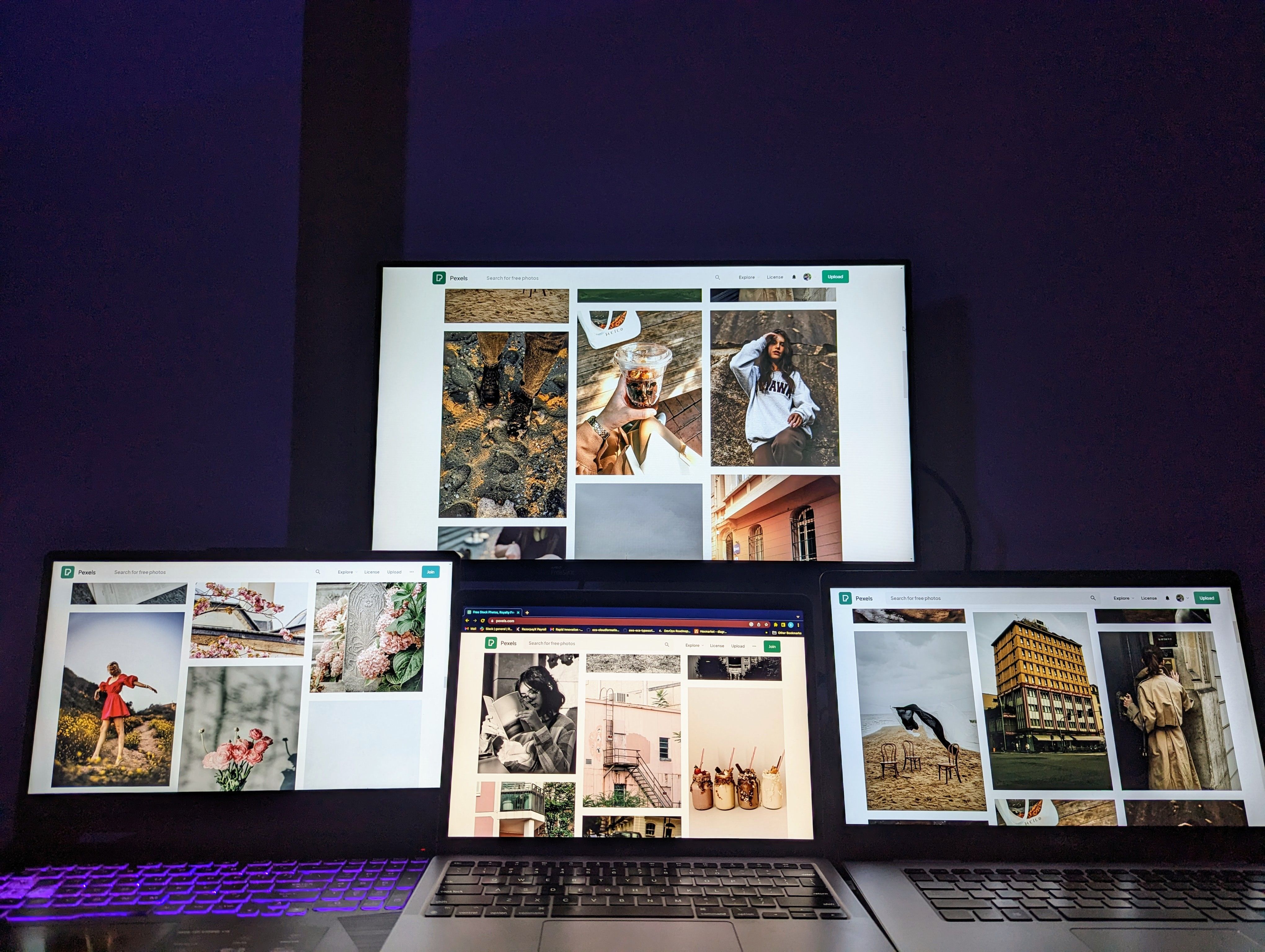 A high-tech workspace featuring three laptops and a monitor with various images displayed, highlighting technology and digital art.