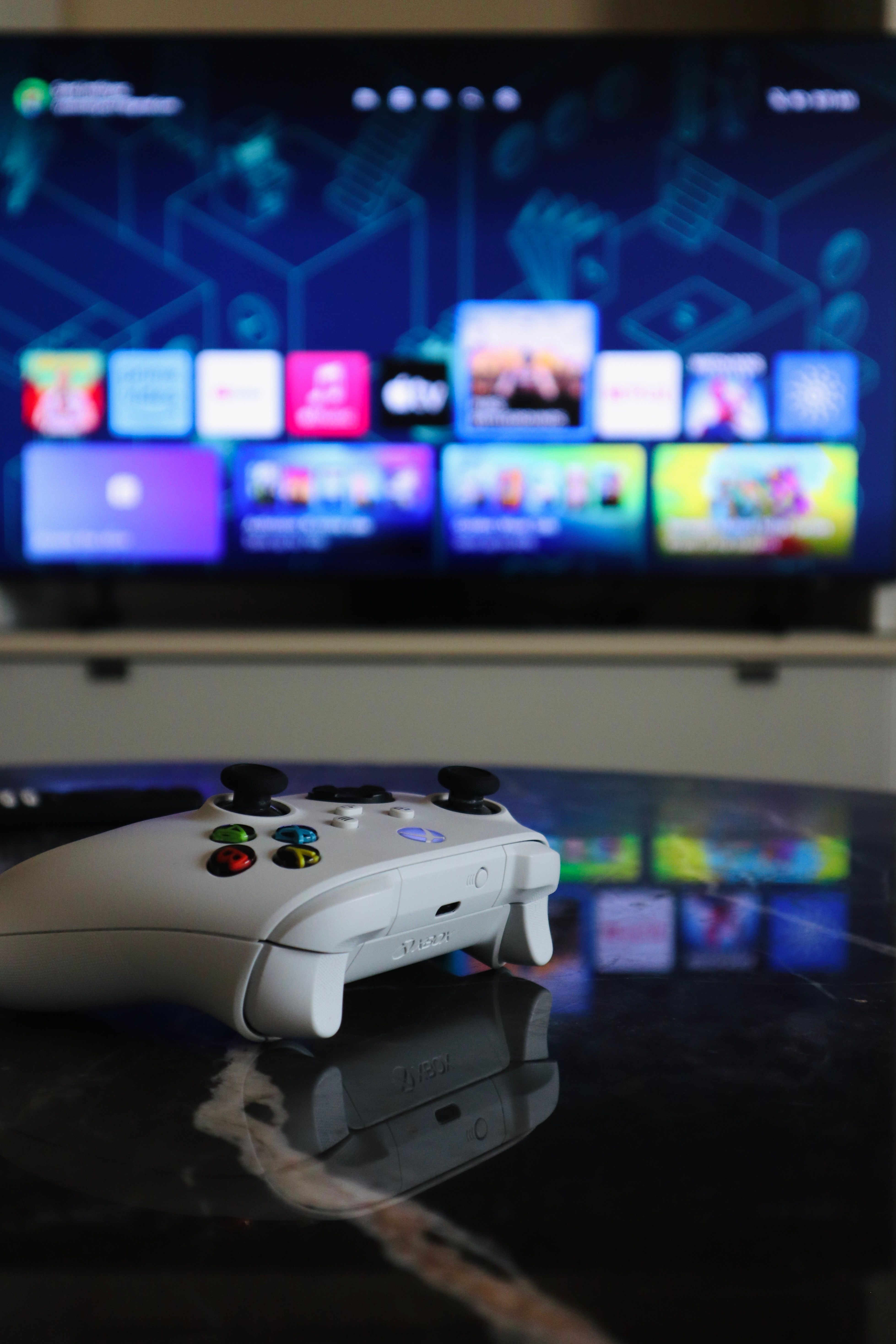 A white gaming controller on a marble table with a TV displaying a vibrant gaming interface in Sharjah home.