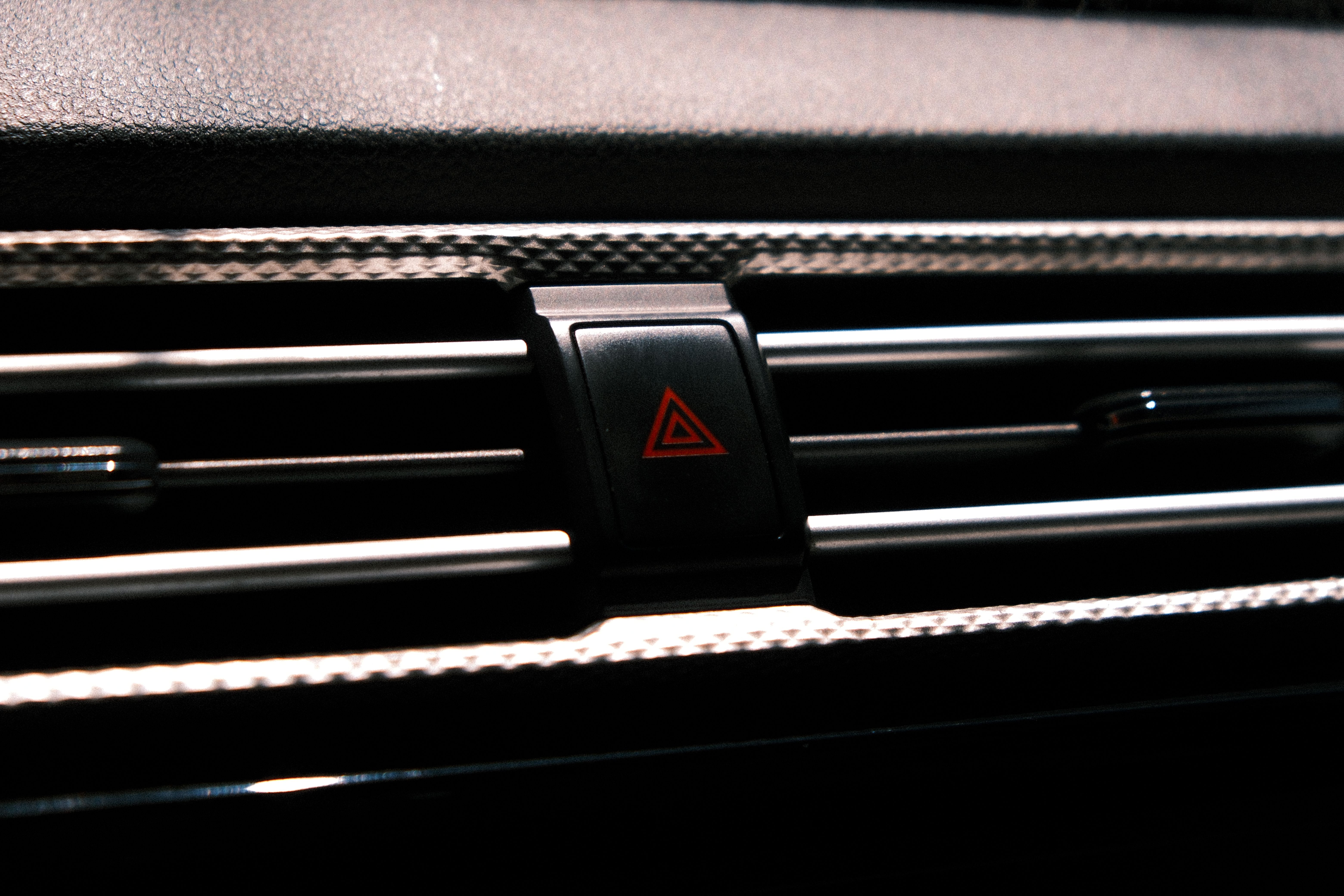 Close-up image of a car hazard light button on a dark dashboard.