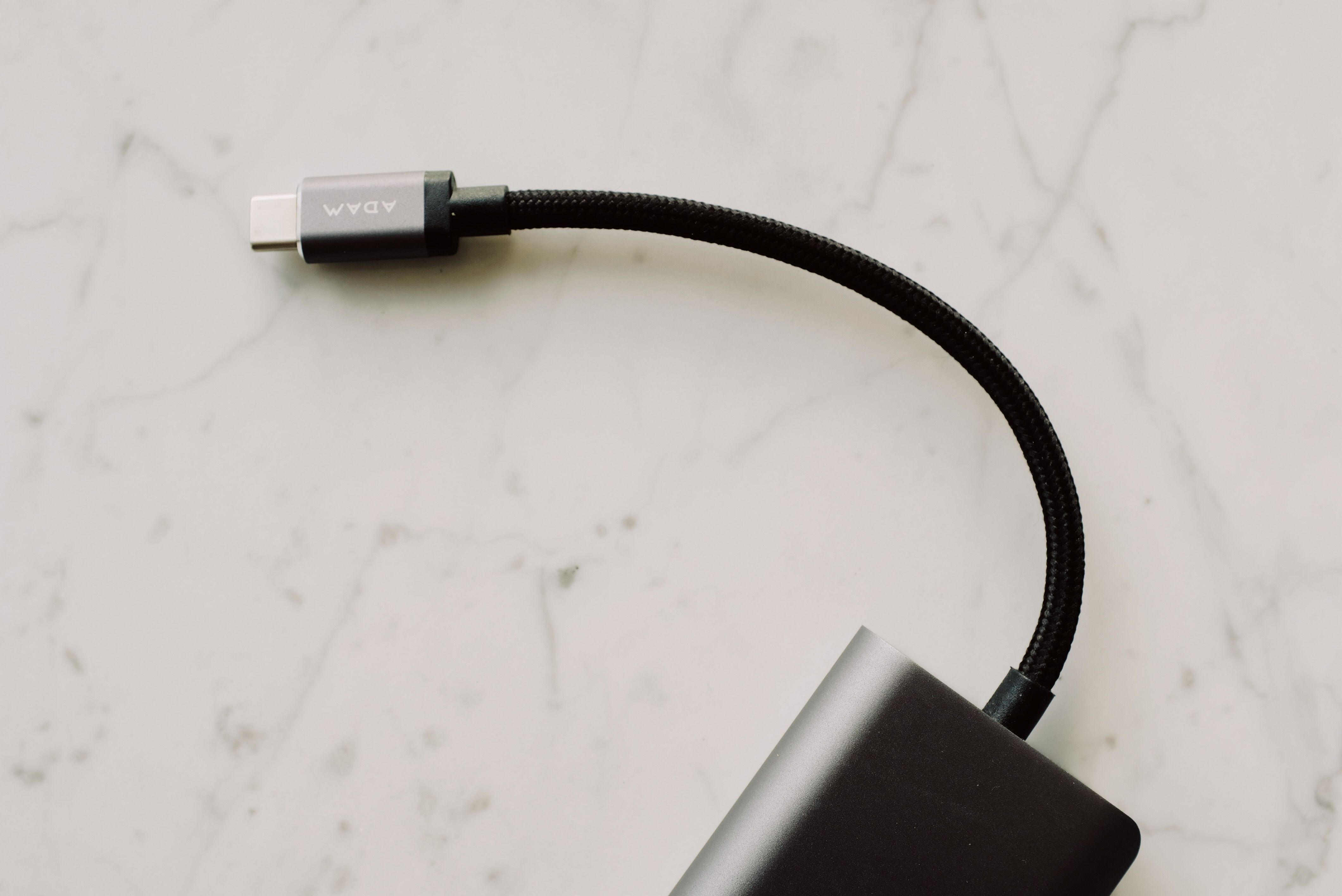 A close-up view of a black USB-C cable with a braided cord resting on a light marble surface.