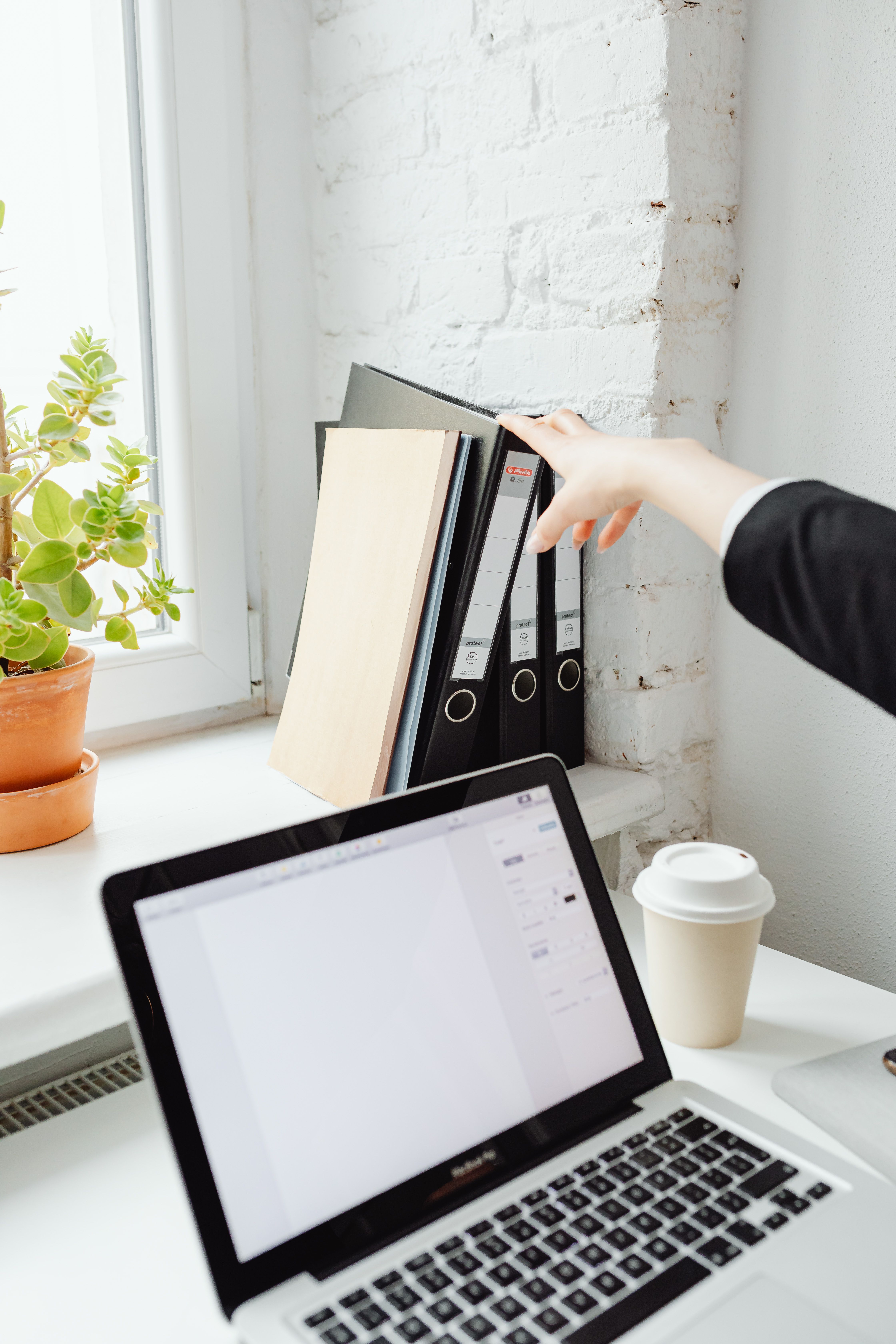 A modern office workspace with a laptop, coffee cup, and folders on a desk.